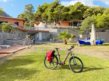 Ein Mietfahrrad von Sicula Bike steht auf dem Rasen vor einigen Ferienhäusern.