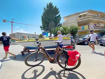 Ein Mietfahrrad von Sicula Bike steht vor einem Boot, das vier Männer auf der Strasse rollen lassen.