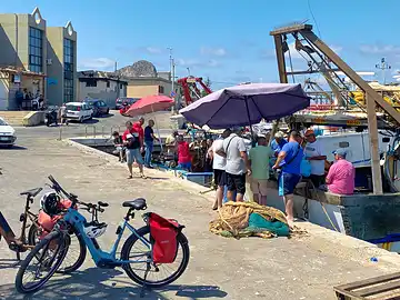 Ein Fahrrad steht auf dem Pier des Hafens von Porticello vor einem Trawler, an dem Fisch verkauft wird.