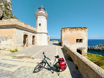 Un vélo est garé devant le phare, à l'extrémité du Capo Zafferano.