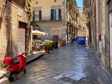 Eine Vespa, eine Ape und der Aussenbereich eines Restaurants in der Via Alessandro Paternostro in Palermo.