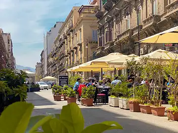 Menschen sitzen entspannt an Tischen vor Restaurants auf der Fussgängerzone 'Via Emerico Amari' in Palermo.