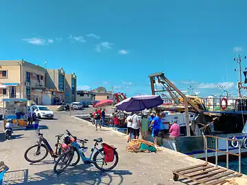 Ein Fahrrad steht auf dem Pier des Hafens von Porticello vor einem Trawler, an dem Fisch verkauft wird.