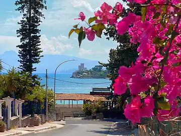 Der Weg zum Lido Olivella von Porticello mit bunten Blüten im Vordergrund und Meer und Bergen im Hintergrund.