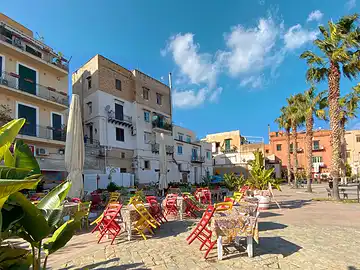 Stühle und Tische im Aussenbereich eines Restaurants auf der Piazza des Hafens von Porticello.